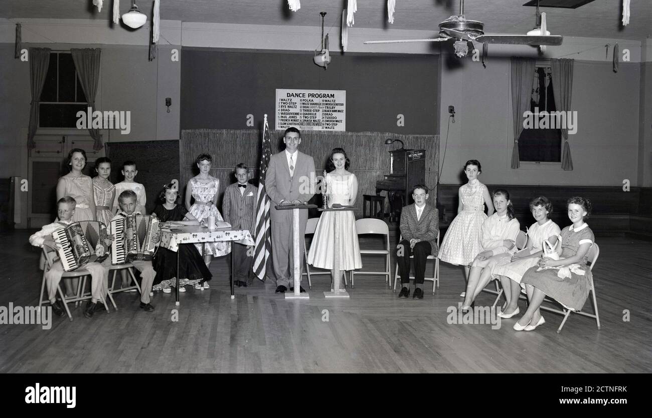 Early 1950s, historical picture of children sitting in a line in a hall, some holding trophies, having competed in a musical dance contest, which were popular in this era. The sign for 'Dance Program', lists traditional 27 dances including the Waltz, two-step and Polka. A notice on the piano says' This is an Old Time Dance' No jitterbug dances allowed! Stock Photo