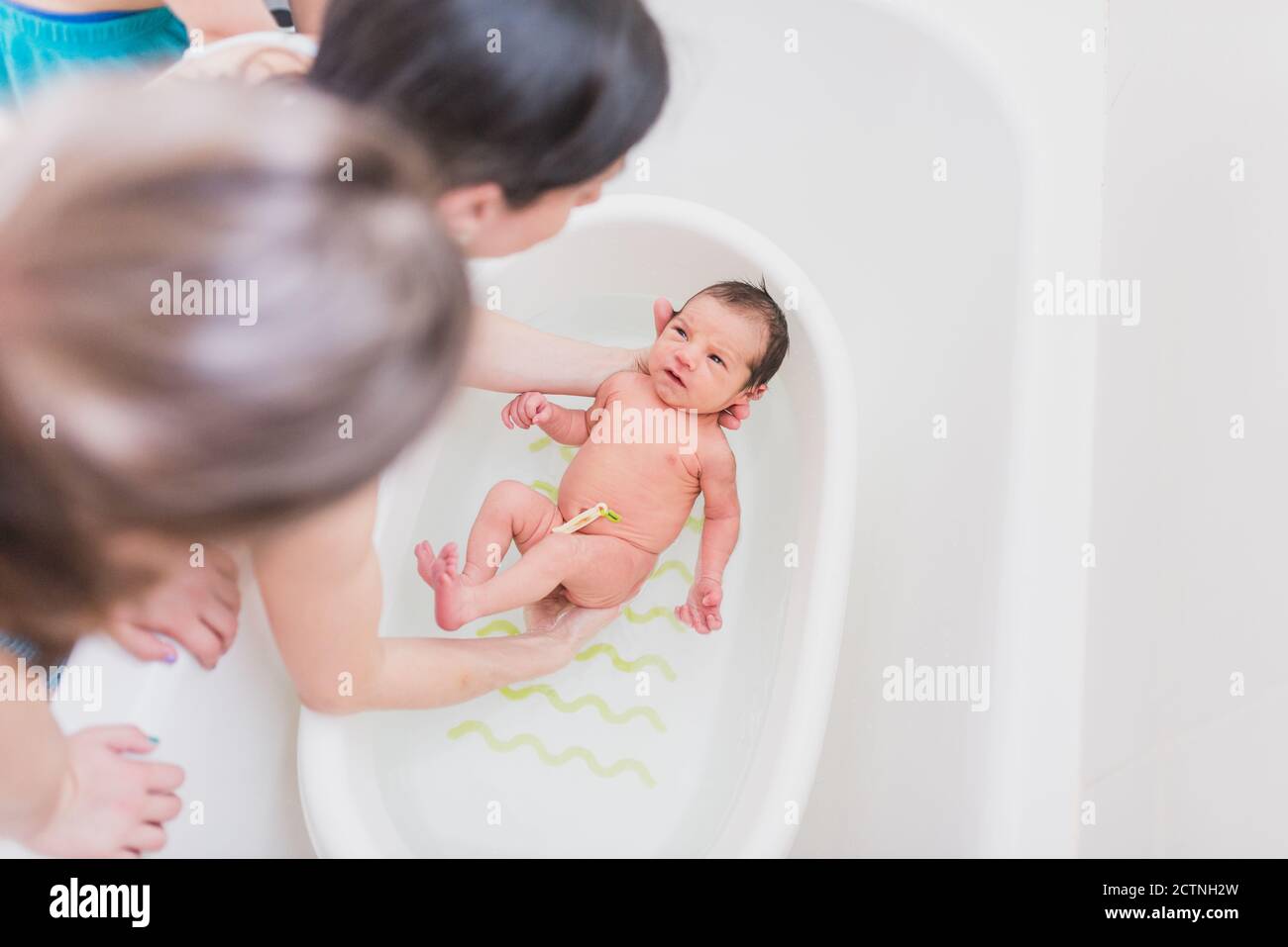 From above unrecognizable parent and kid washing crying newborn baby in
