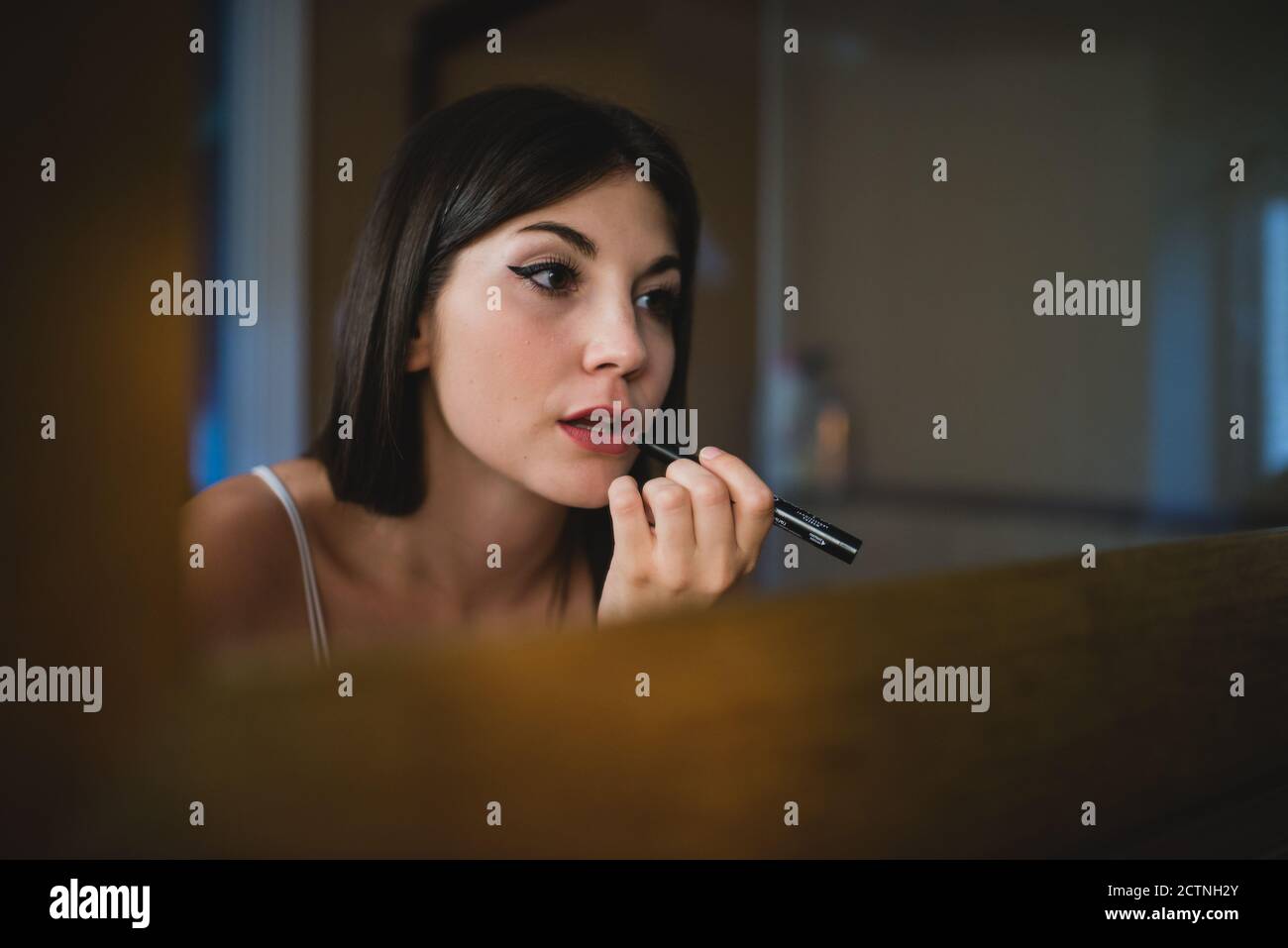 Concentrated charming female with smooth skin applying red lipstick while preparing for event Stock Photo