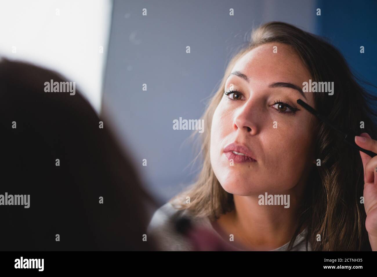 Concentrated charming female with smooth skin applying mascara while preparing for event Stock Photo
