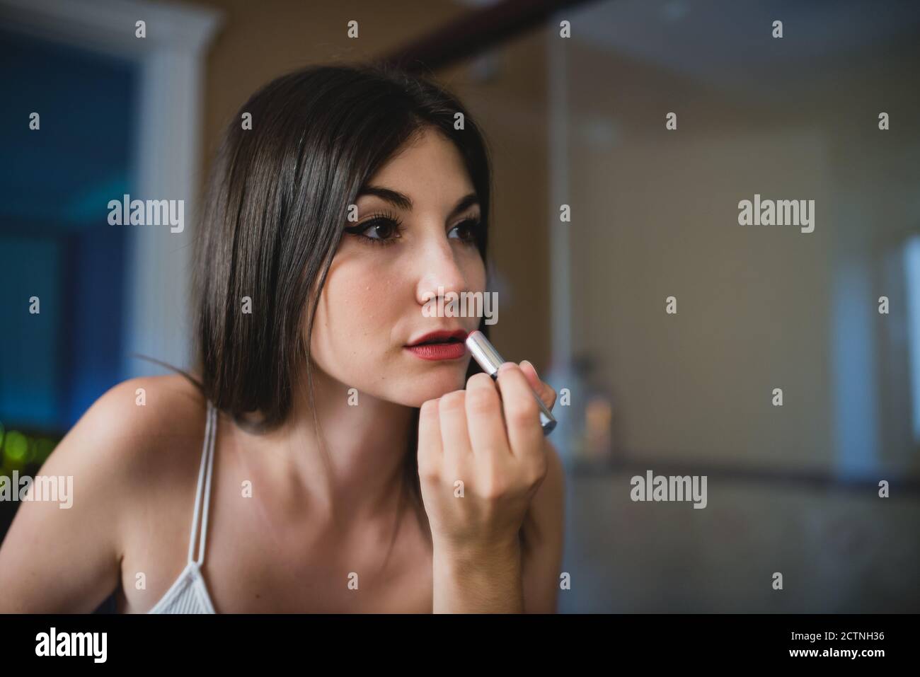 Concentrated charming female with smooth skin applying red lipstick while preparing for event Stock Photo
