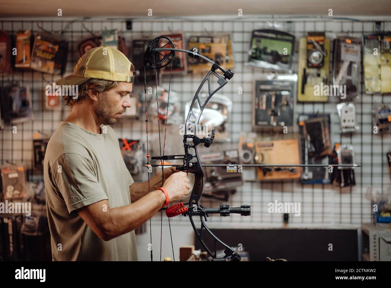 Side view of busy male hunter adjusting compound bow with arrow while