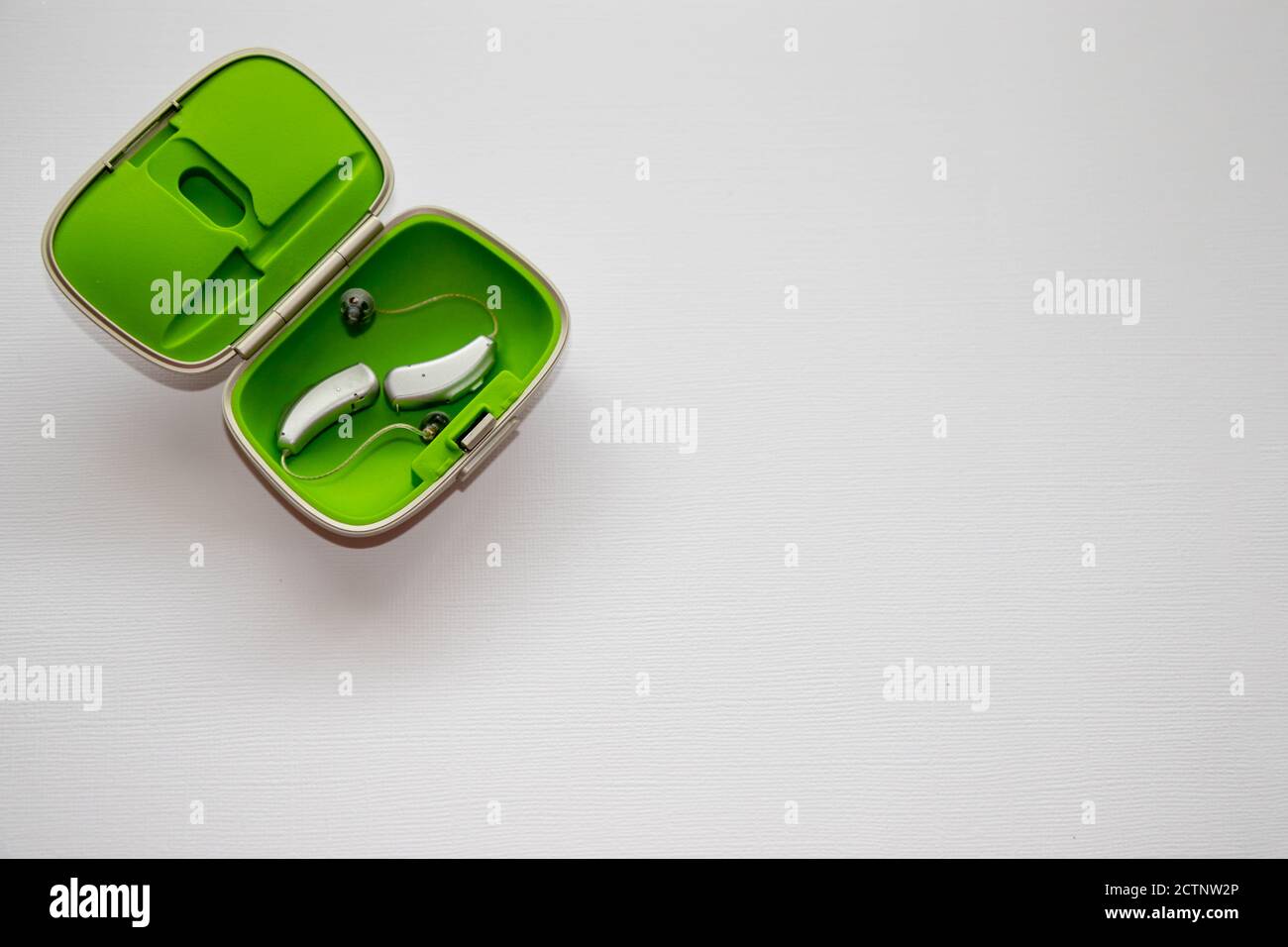 Two BTE (behind the ear) hearing aids in green container box on white