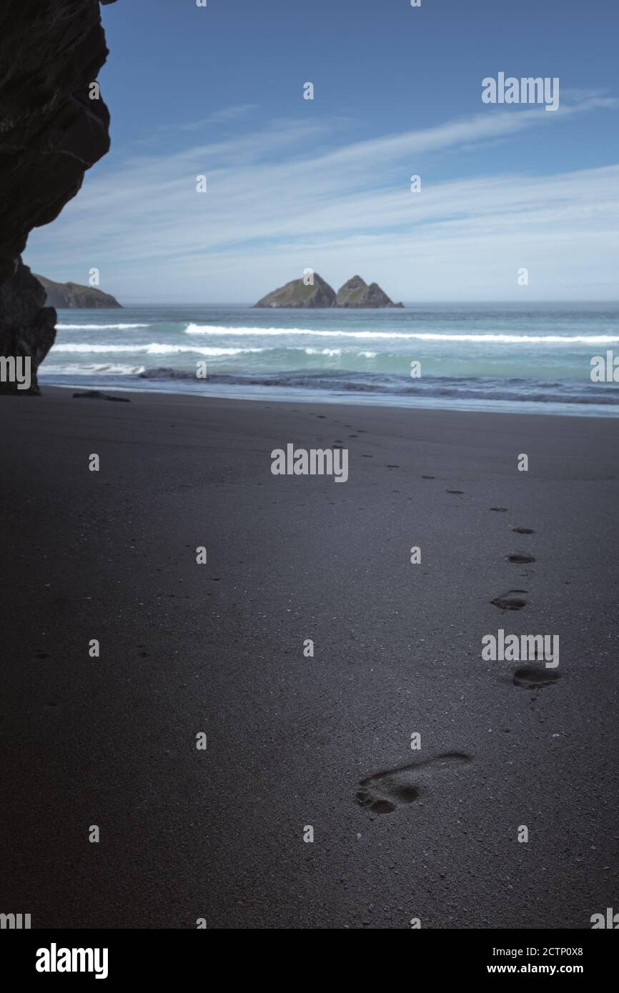 Footprints in the sand and the view of Gull Rock form Holywell Cave on Holywell Bay Beach Stock Photo