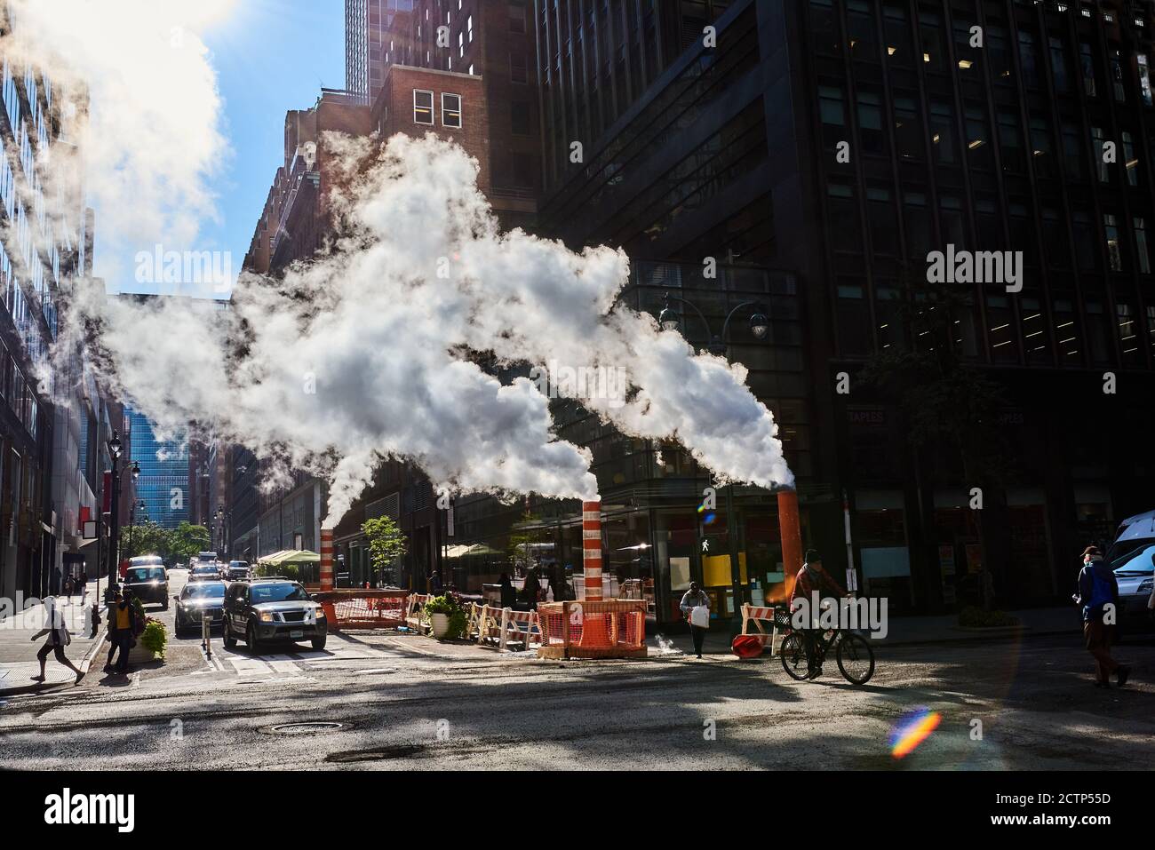 Back-lit photo of steam vapor being vented through orange and white stacks in midtown Manhattan, NYC Stock Photo