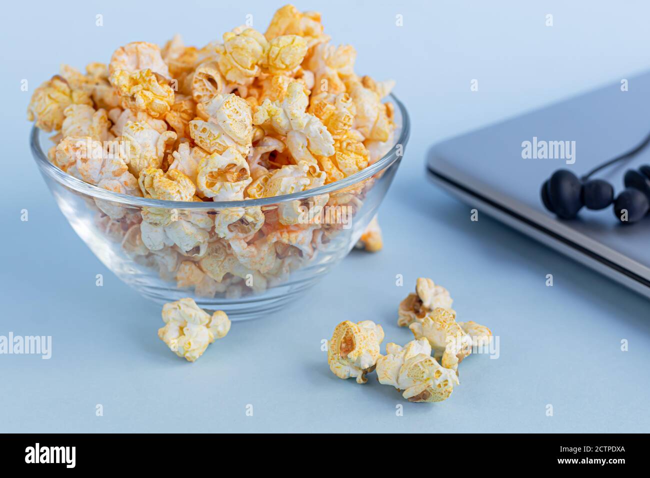 A transparent bowl of popcorn on a blue surface. Next to a laptop and