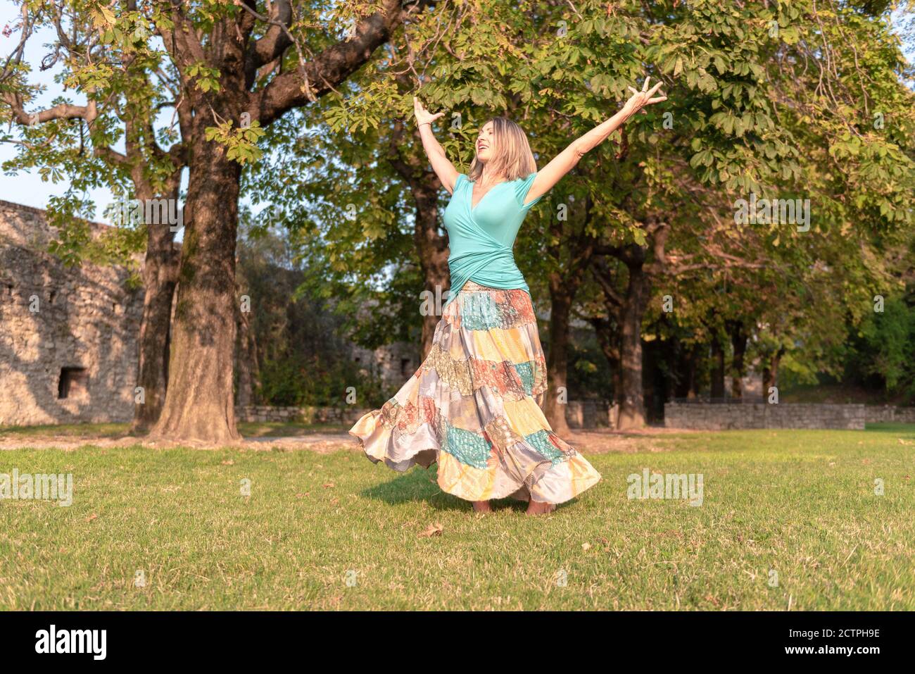 Beautiful barefoot girl in a long colorful skirt is dancing in natural background Stock Photo
