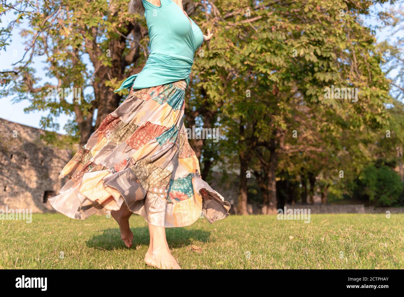 Beautiful barefoot girl in a long colorful skirt is dancing in natural background Stock Photo