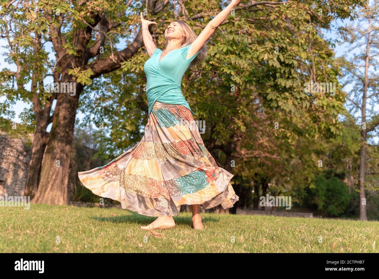Beautiful barefoot girl in a long colorful skirt is dancing in natural background Stock Photo
