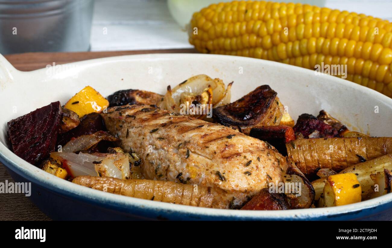 A grilled chicken is sitting in a ceramic plate alongside various root vegetables. Charred lines from the skillet pattern are clearly visible. Stock Photo