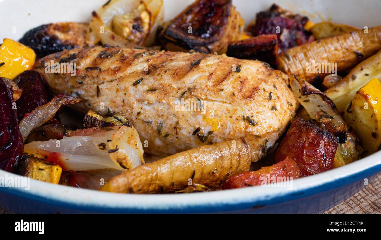 A grilled chicken is sitting in a ceramic plate alongside various root vegetables. Charred lines from the skillet pattern are clearly visible. Stock Photo