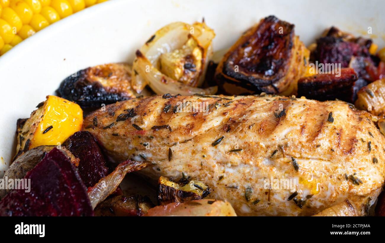 A grilled chicken is sitting in a ceramic plate alongside various root vegetables. Charred lines from the skillet pattern are clearly visible. Stock Photo