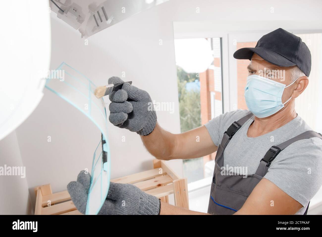 Brush cleaning Air conditioner from dust. Worker in gloves and medical mask checks filter Stock Photo