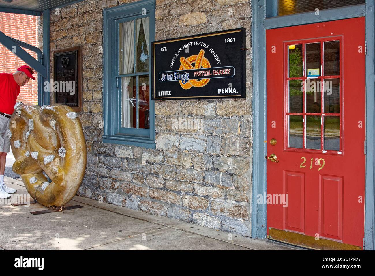 Julius Sturgis Pretzel Bakery, old stone building, red door, blue trim, large pretzel replica, man looking, America's First Pretzel Bakery, 1861, Lanc Stock Photo