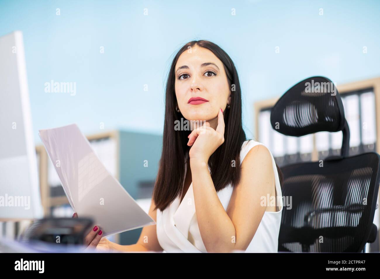 Business woman sitting at desk, holding document Stock Photo
