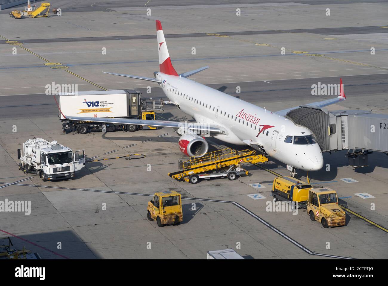 An Austrian Airlines passenger jet aircraft parked at Heathrow Airport with support vehicles adjacent and an air bridge connected Stock Photo