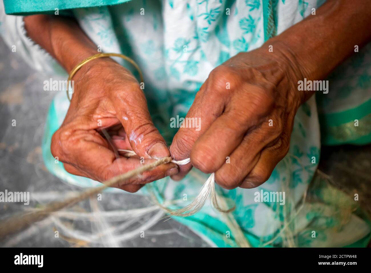 An old age woman is making on his skinny hands a rope from the banana