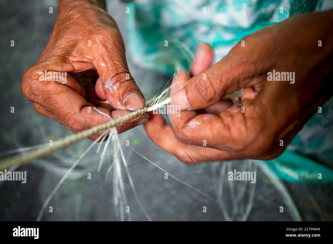 An old age woman is making on his skinny hands a rope from the banana