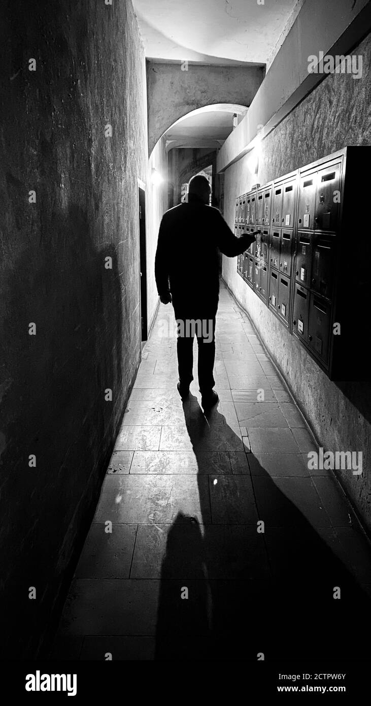 Silhouette of a male checking the mailbox in the dark corridor of the apartment building Stock Photo