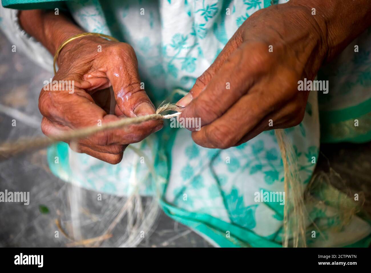 An old age woman is making on his skinny hands a rope from the banana
