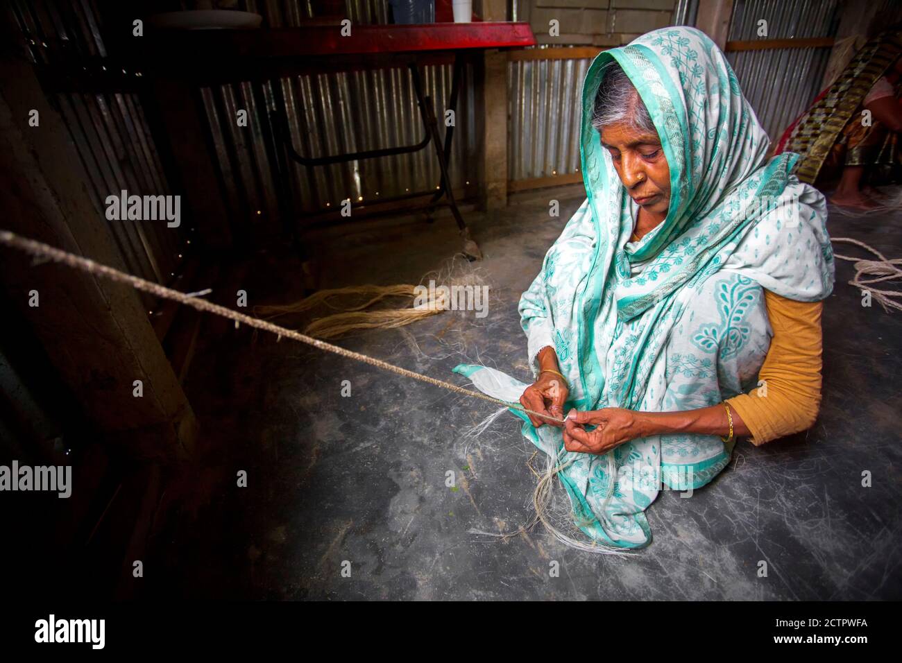 An old age woman is making a rope from the banana tree fibers in her