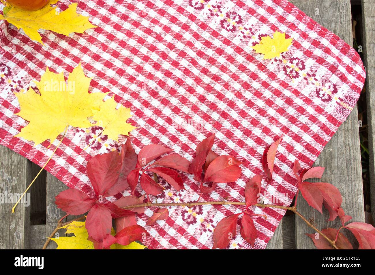 Autumn background, red tablecloth on a wooden table, yellow and red leaves Stock Photo