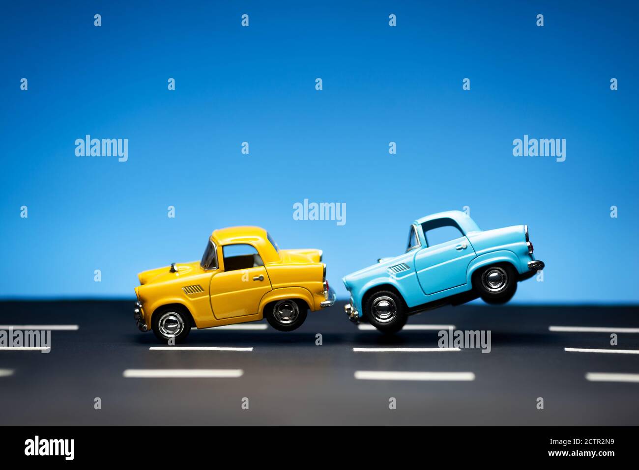 Yellow toy car and a blue car on a blue background and on a road. Blue