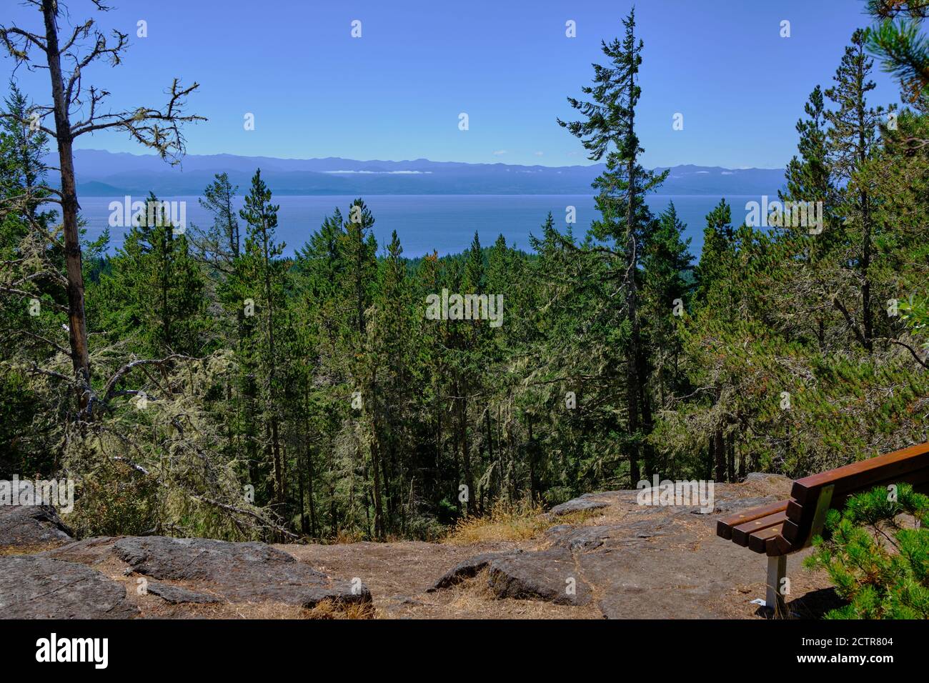 Wooden bench near summit of Mount Maguire provides views over forests of Sooke, BC and the strait of Juan de Fuca to Washington's Olympic Mountains Stock Photo