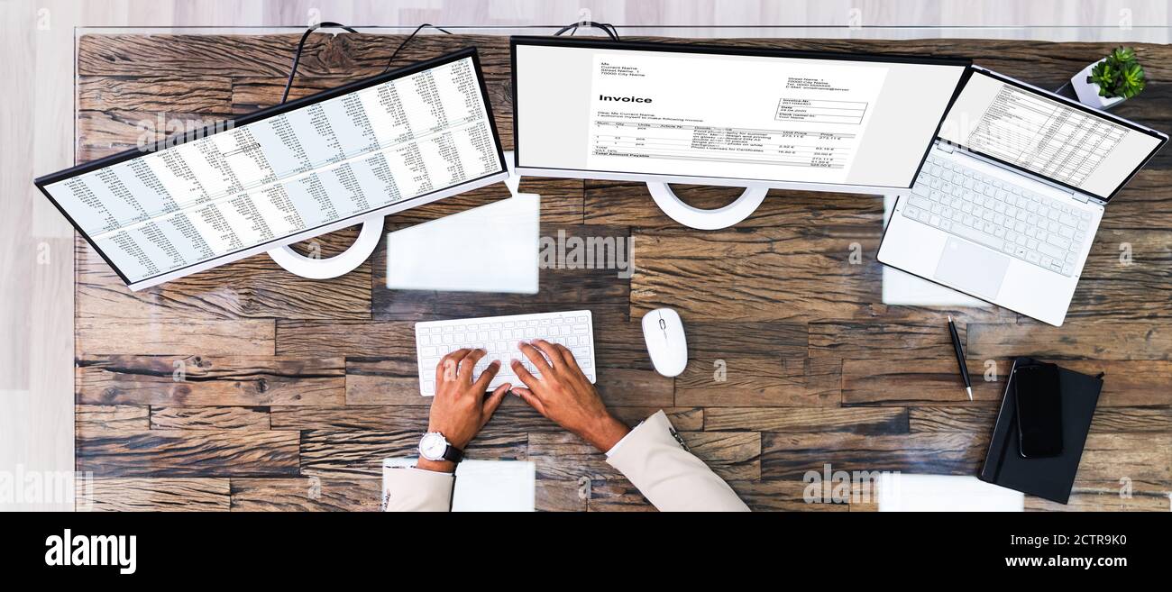 Looking At Invoice And Spreadsheet On Computer At Work Stock Photo