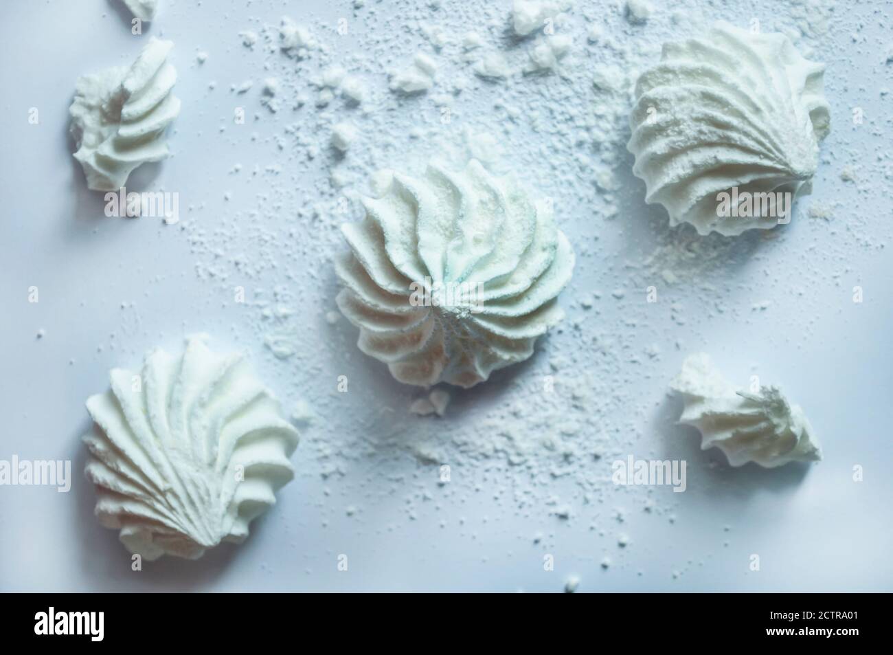 Three white air meringues lie diagonally on a white background. Next to them crumbs of broken meringue. The effect of lightness, fragility Stock Photo