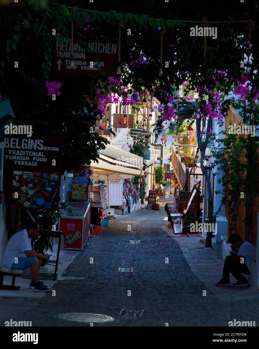 A narrow cobbled street with restaurants and shops leading down to the sea front at Kalkan in Turkey.  Kalkan is a popular holiday destination and is Stock Photo