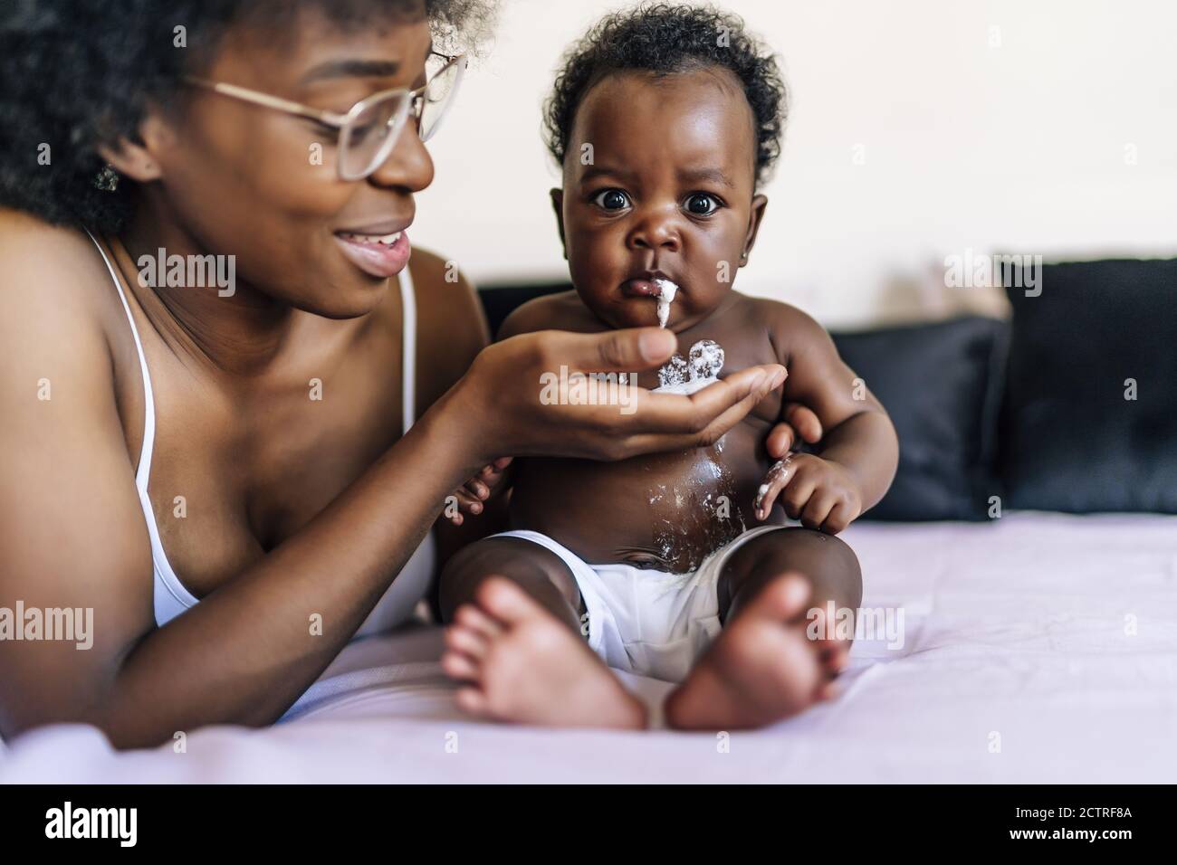 Adorable AfricanAmerican baby vomiting milk in her mother's hand Stock