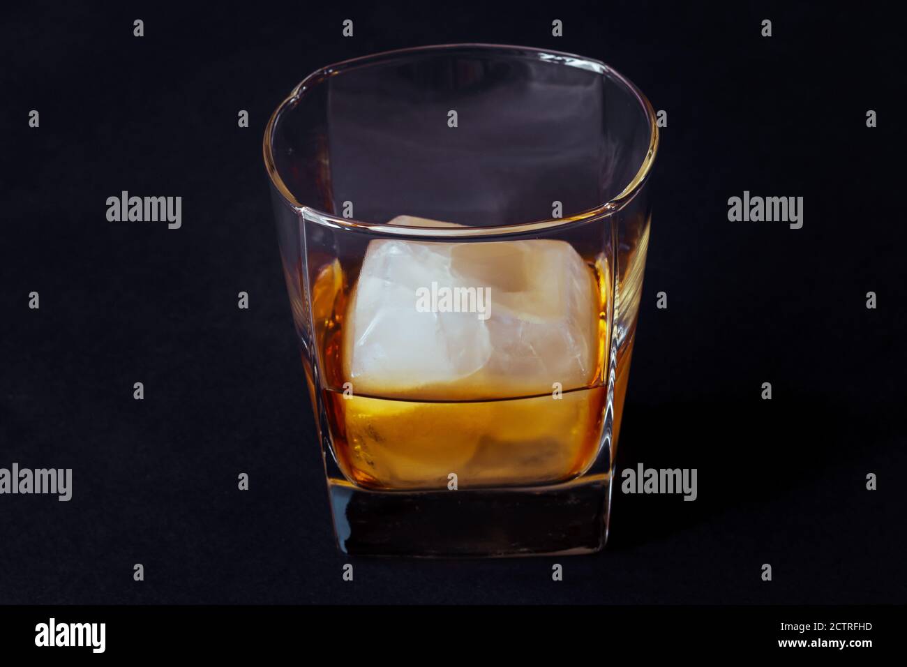 Glass of alcoholic drink with ice cube on black table. Whiskey in glass ...