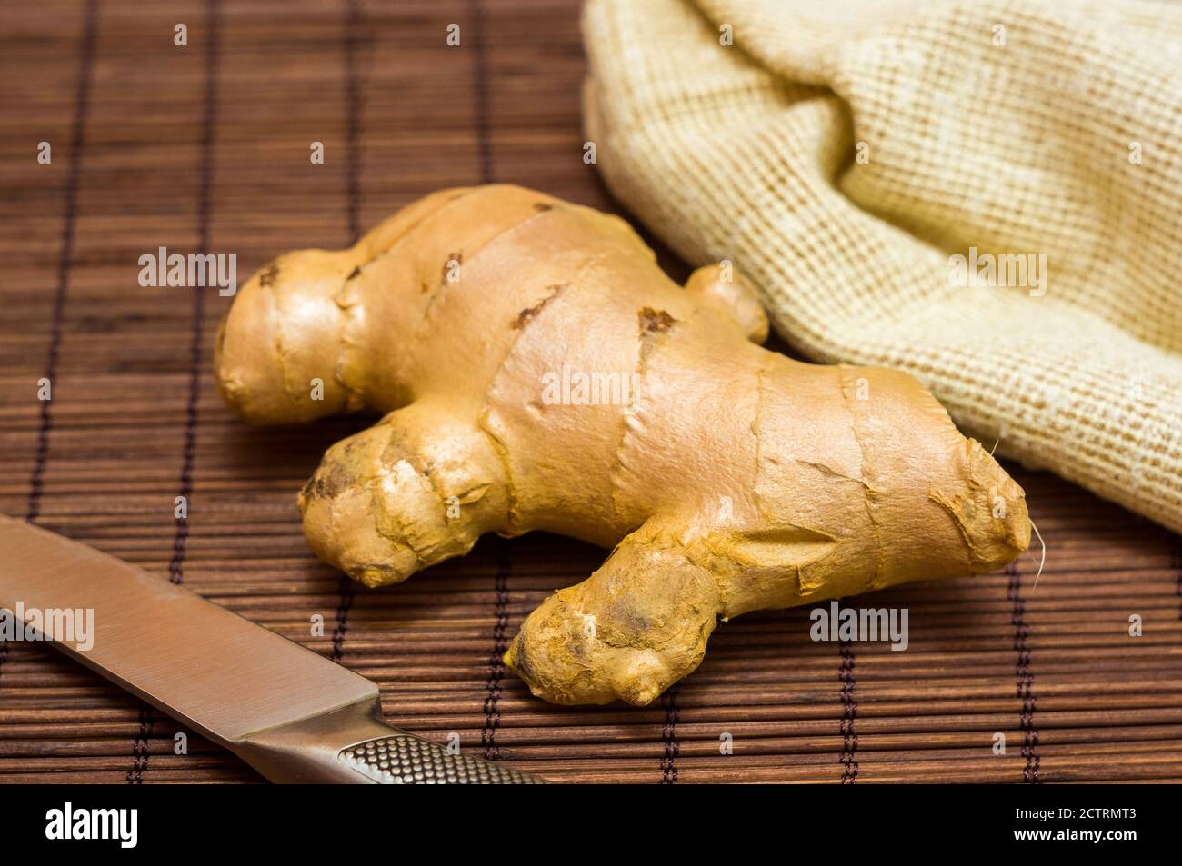 fresh ginger root on bamboo mat with knife and napkin, close-up Stock Photo