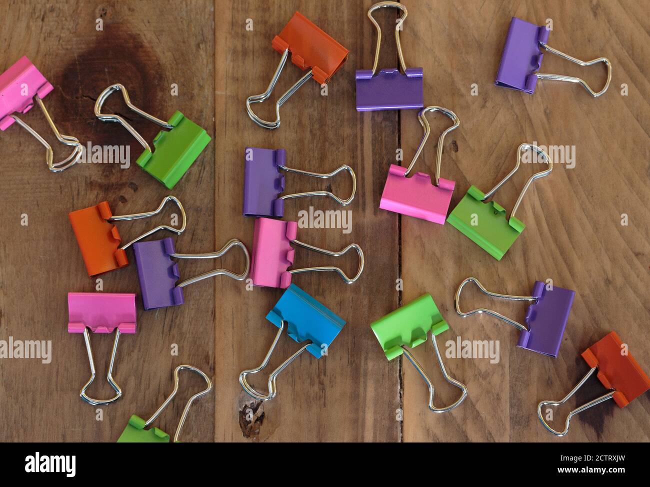 assorted binder clips in bright orange, pink, green, purple and blue colors scattered on a wood background Stock Photo