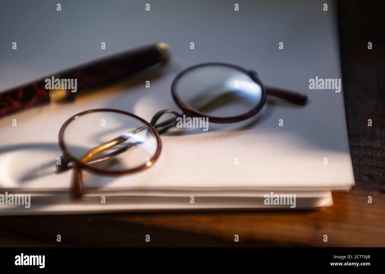 Retro eyeglasses and pen on stack of paper Stock Photo