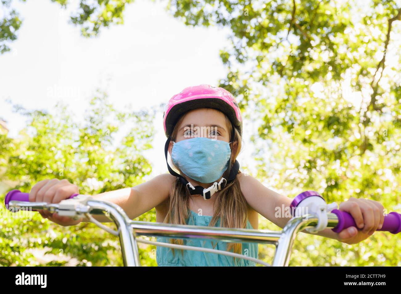 Girl (6-7) wearing flu mask and riding bicycle Stock Photo