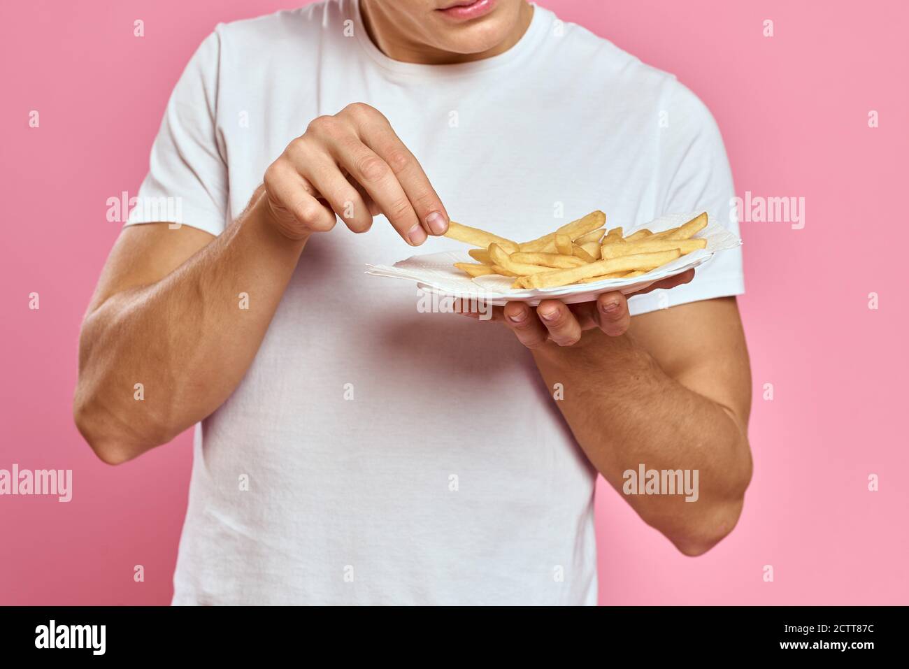 Man with French fries in a paper box on a pink background calories fast