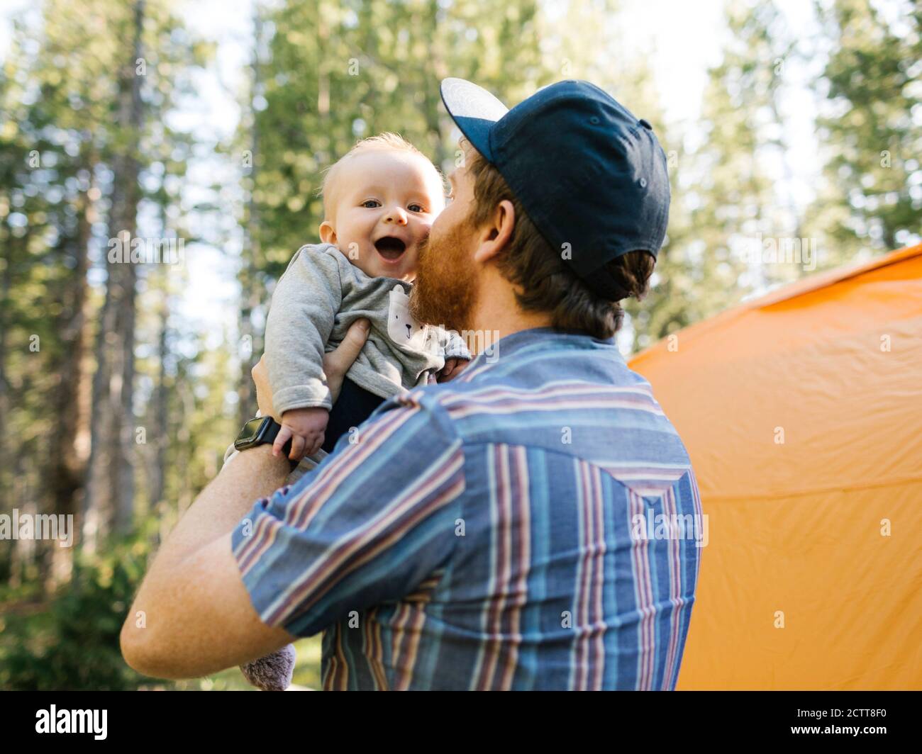 Man kissing baby son (6-11 months) in forest, tent in background, Wasatch Cache National Forest Stock Photo
