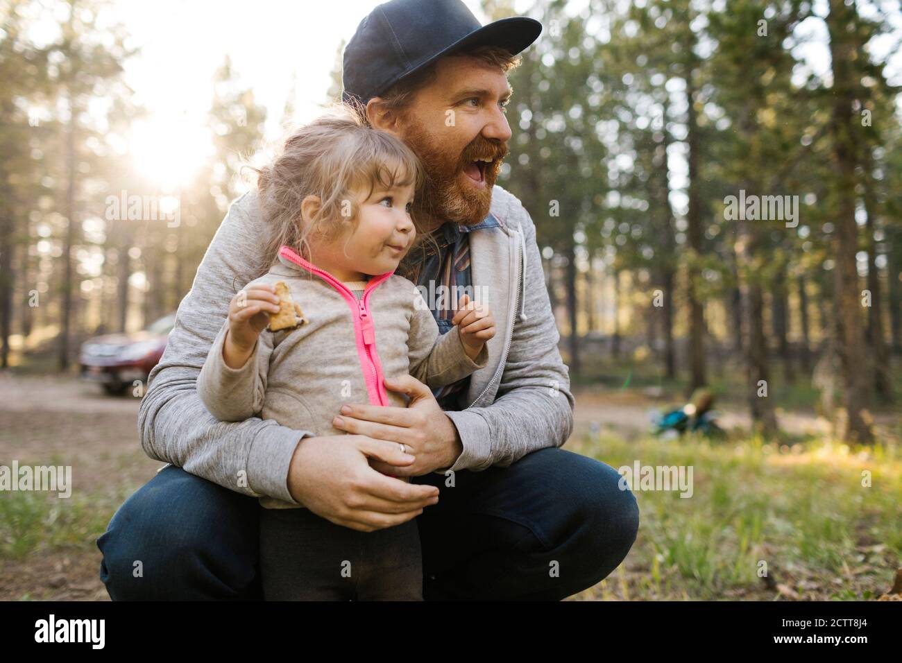 Smiling man with daughter (2-3) on laps in forest, Wasatch Cache National Forest Stock Photo