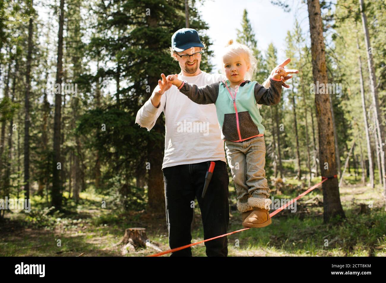 Father assisting daughter (2-3) walking on slackline in forest, Wasatch-Cache National Forest Stock Photo