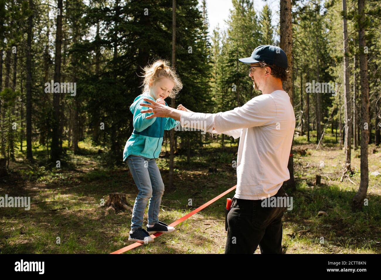 Father assisting daughter (2-3) walking on slackline in forest, Wasatch-Cache National Forest Stock Photo