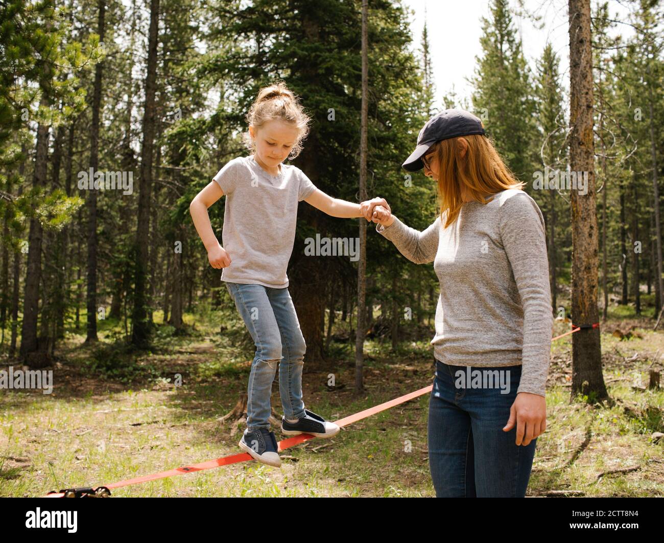 Mother assisting daughter (6-7) walking on slackline in forest, Wasatch-Cache National Forest Stock Photo