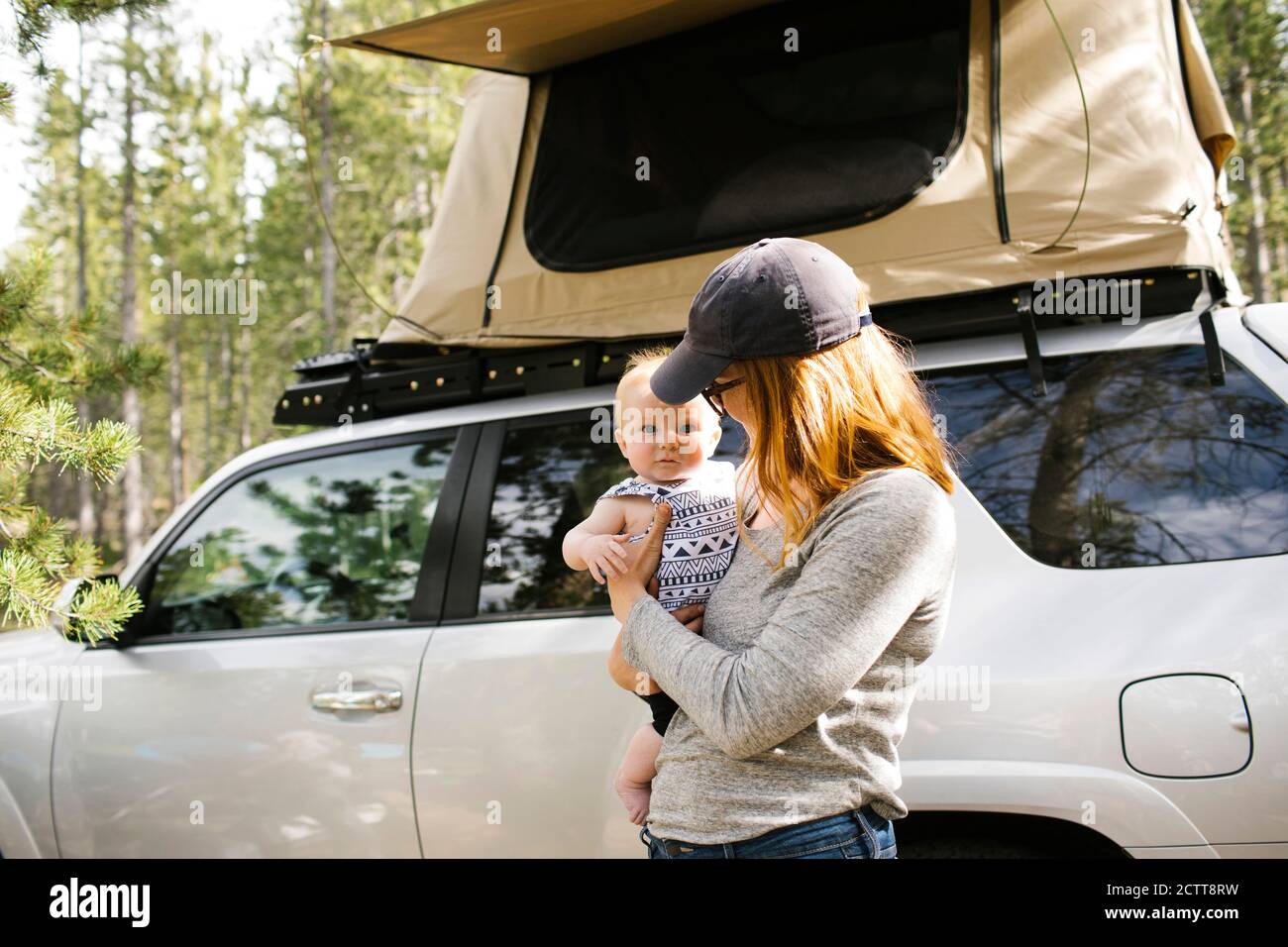 Woman holding baby son (6-11 months) on camping, car with tent in background, Wasatch Cache National Forest Stock Photo
