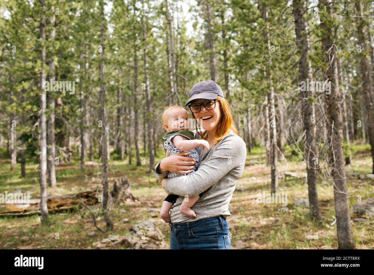 Portrait of smiling woman holding baby son (6-11 months) in forest, Wasatch Cache National Forest Stock Photo