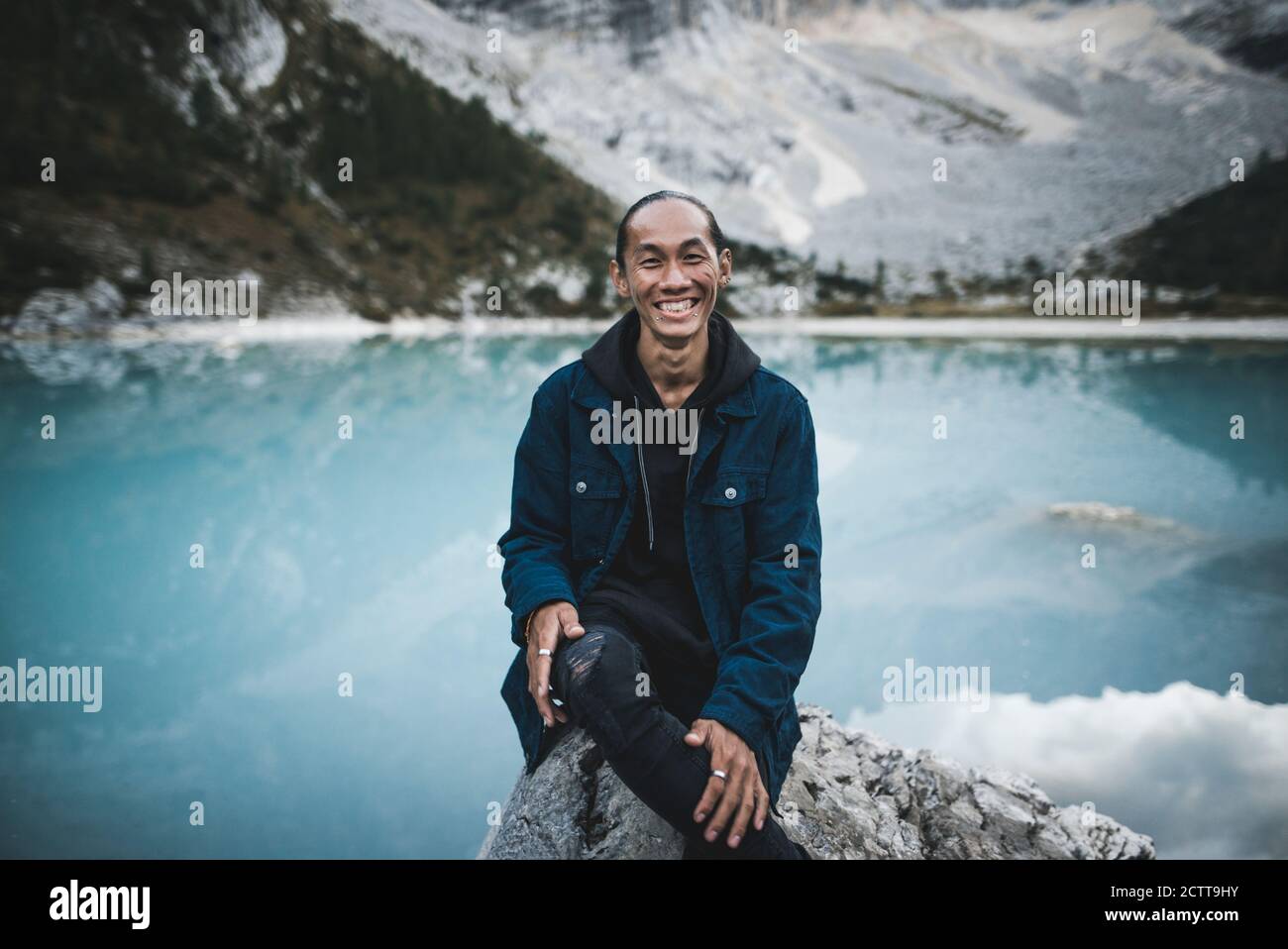 Italy, South Tyrol, Cortina d Ampezzo, lake Sorapis, Portrait of young man sitting on rock at mountain lake Stock Photo