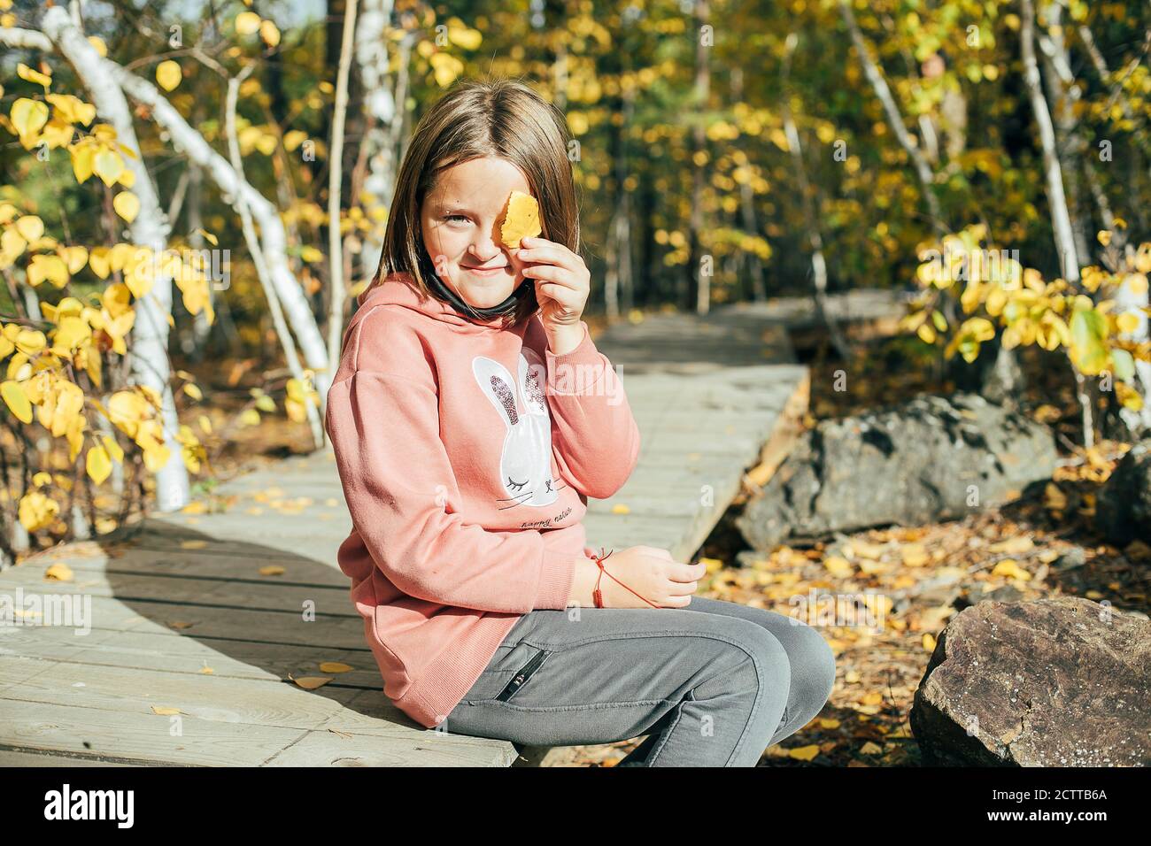 Cute girl covering face with a yellow leaf while smiling against Stock ...