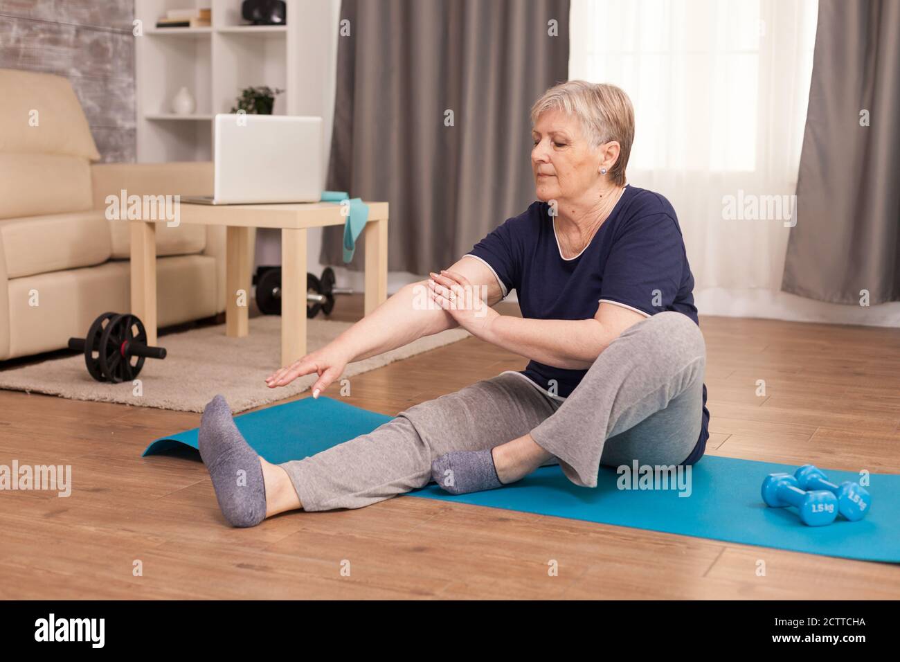 Senior healthy woman practicing fitness at home. Old person pensioner online internet exercise training at home sport activity with dumbbell, resistance band, swiss ball at elderly retirement age Stock Photo