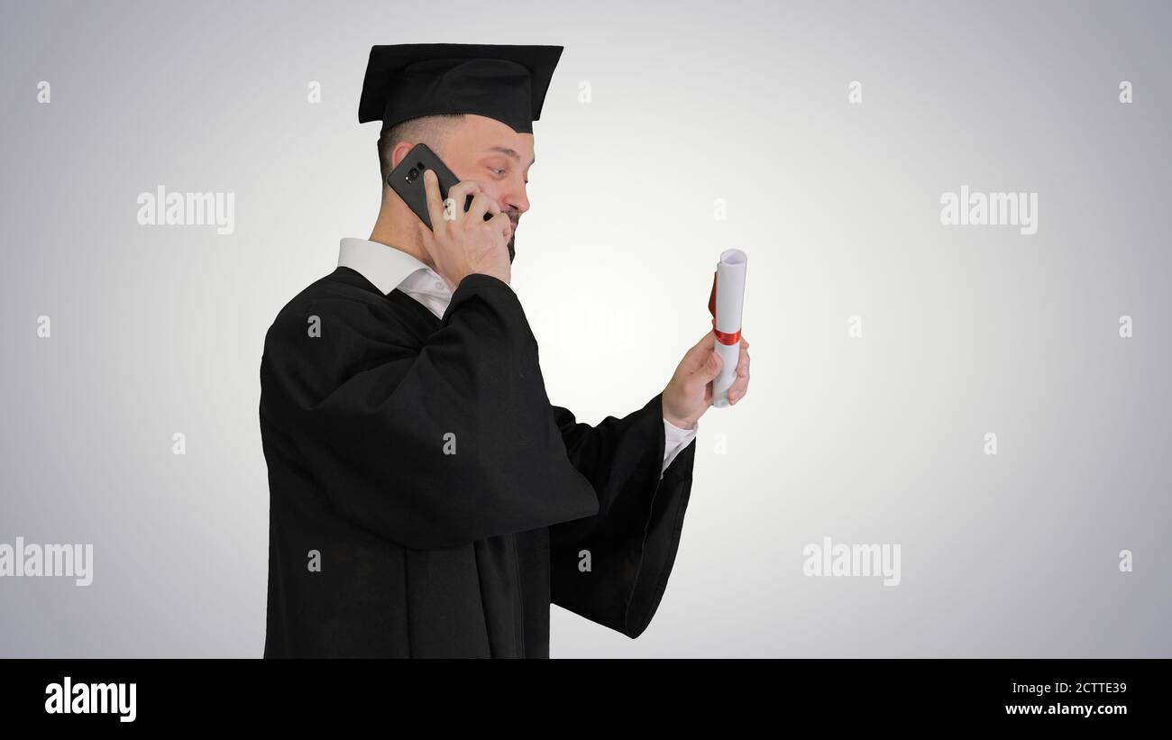 Graduating student walking and making a call on gradient backgro Stock Photo