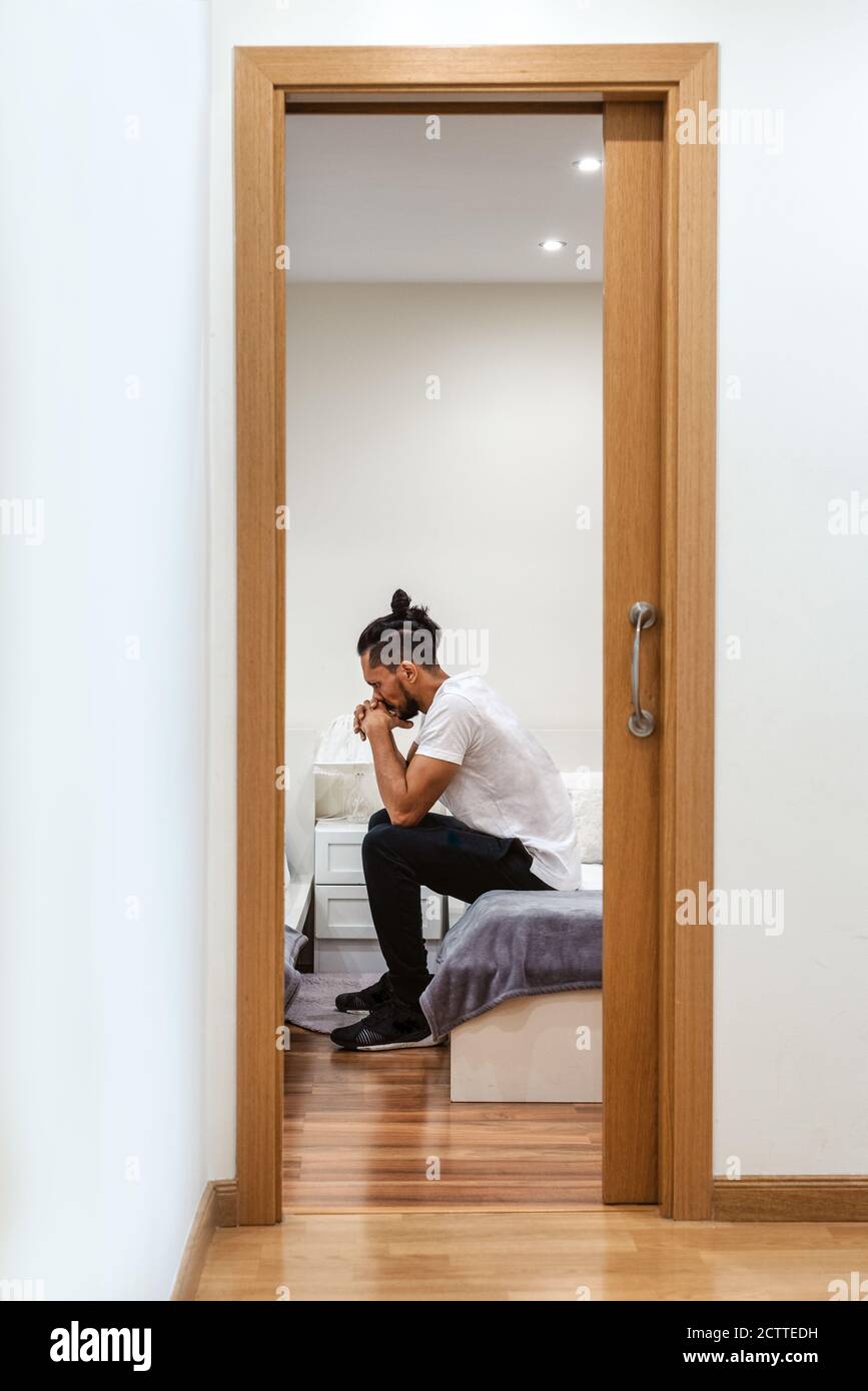 Hispanic man sitting on a bed and thinking Stock Photo